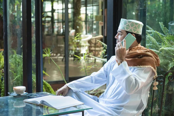 Árabe musulmán hombre de negocios utilizar la comunicación de teléfonos inteligentes y escribir en el libro en la cafetería, freelance sin estilo de vida espacio de trabajo . —  Fotos de Stock