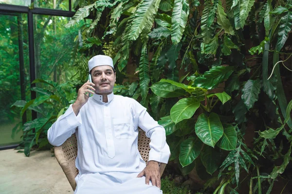 Oriente Médio homem Emirati em roupas tradicionais chamado kandura sentado na cadeira no café e conversando com seu mobile.Smart conceito de tecnologia de comunicação . — Fotografia de Stock