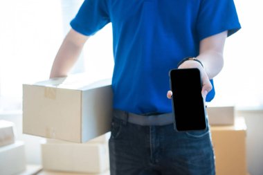 Üniformalı genç teslimatçı elinde akıllı telefonu boş ekranla gösteriyor. Ulaşım teknolojisi kavramı..