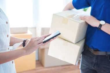 View of young asian woman appending signature in digital smart mobile phone after receiving parcel from courier delivery man at home.AI Technology transportation concept.