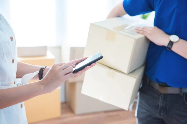 View of young asian woman appending signature in digital smart mobile phone after receiving parcel from courier delivery man at home.AI Technology transportation concept. — Stok fotoğraf