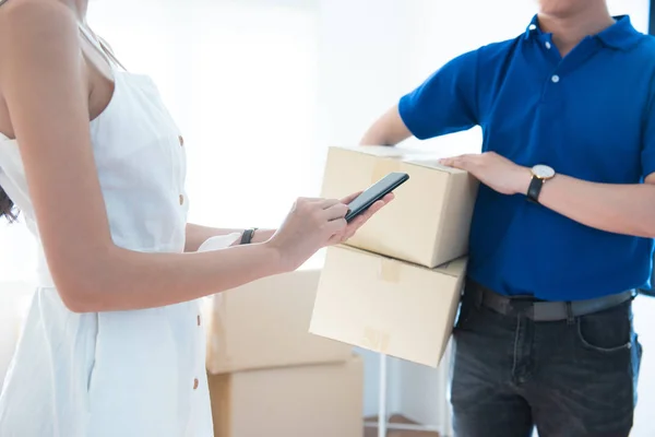 View of young asian woman appending signature in digital smart mobile phone after receiving parcel from courier delivery man at home.AI Technology transportation concept. — Stok fotoğraf