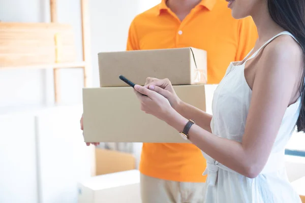 View of young asian woman appending signature in digital smart mobile phone after receiving parcel from courier delivery man at home.AI Technology transportation concept. — Stok fotoğraf