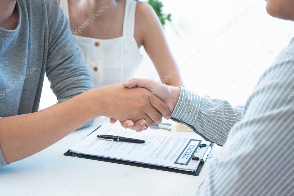 Buying something special. Young loving couple bonding to each other and looking at man sitting in front of them at the desk and holding some document