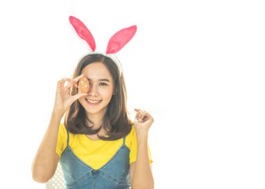 Asyalı güzel, mutlu, tavşan kulağı takan ve gözlerinin önünde renkli bir Paskalya yumurtası tutan neşeli genç bir kadının çekimleri. Sevimli bir gülümseme ve renkli bir dekor kostümü..