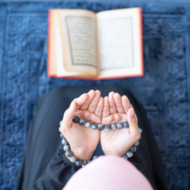 Asyalı genç ve güzel Müslüman kadının yanında tespih çekip Kuran okuyan camide meditasyonla halıya oturmuş..
