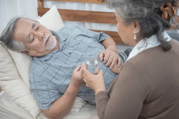 Asya 'lı kıdemli adam evde kanepede yatarken ilaç ve içme suyu alırken, fotokopi alanı ile sağlık ve tıp konsepti.