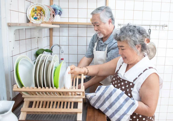 Happy asian elder senior couple washing dishes in sink at home in kitchen at home.