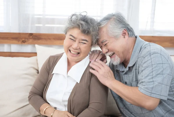 Romantic and happy asian elder senior couple laughing while sitting on sofa at home