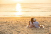A szerelmesek együtt nézik a naplementét a nyári vakációkon. Emberek sziluett hátulról ülve élvezi kilátás naplemente tenger trópusi úti cél nyaralás. Romantikus pár a tengerparton.