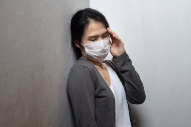 Cerrahi maske takan bayan Asyalı baş ağrısı çeken ve duvara yaslanan hasta ruhlu genç bir kadın beyaz arka planda izole edildi. Wuhan Coronavirus (Covid-19) salgını önleme. Sağlık hizmeti kavramı