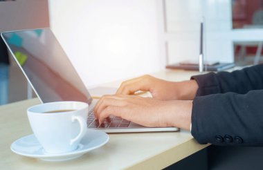 Asyalı iş adamı elleri dizüstü bilgisayarın klavyesinde iş grafiği çizelgesi veri formları, cep telefonu ve modern merkez ofisin masasında bir fincan kahve yazıyor. Dijital pazarlama kavramı.