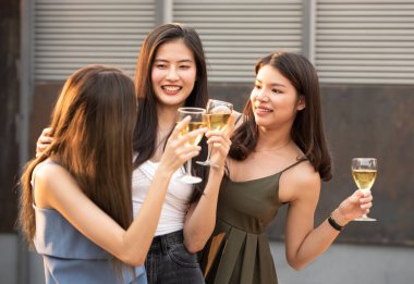 Bir grup güzel, mutlu Asyalı kadın ellerinde şarap kadehiyle arkadaşlarıyla sohbet ederken açık çatı klübünde dans partisini kutluyorlar. Genç arkadaşlığın eğlence yaşam tarzı konsepti..