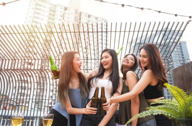 Bir grup Asyalı genç kız arkadaş, gece kulübünde elinde bir şişe birayla dans partisini kutlarken mutlu oluyor..