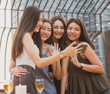 Genç Asyalı çift aşıkları gece partisinde eğleniyor ve içiyor çatıdaki gece kulübünde ellerinde bira şişesi ve göz teması ile kameralı telefona bakıyorlar..