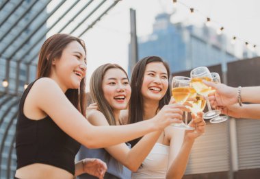 Bir grup güzel, mutlu Asyalı kadın ellerinde şarap kadehiyle arkadaşlarıyla sohbet ederken açık çatı klübünde dans partisini kutluyorlar. Genç arkadaşlığın eğlence yaşam tarzı konsepti..