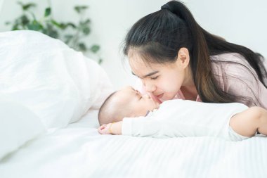 Genç ve güzel Asyalı anne, yeni doğmuş bebeği yatakta öpüyor. Sağlık ve sağlık hizmetleri. Asyalı kız yaşam tarzını seviyor. Asya Anneler Günü afişi ve reklam için fotokopi alanı