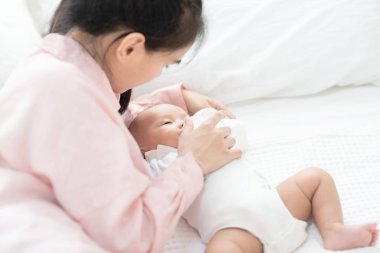Aile, çocuk ve ebeveynlik kavramı. Mutlu, genç, Asyalı anne gülümseyen, yeni doğmuş bebeği kucağına alan ve evde yatağında süt besleyen. Reklam için kopyalama alanı olan pankart
