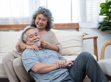 Yaşlı yaşlı Asyalı çiftin evde mutlu bir portresi. Mutlu büyükbaba, evdeki oturma odasındaki kanepede büyükannesine yaslanıyor..