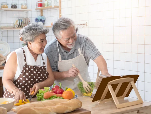 Happy asian elder senior couple cooking fresh meal in kitchen at home.