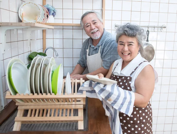Happy asian elder senior couple washing dishes in sink at home in kitchen at home.