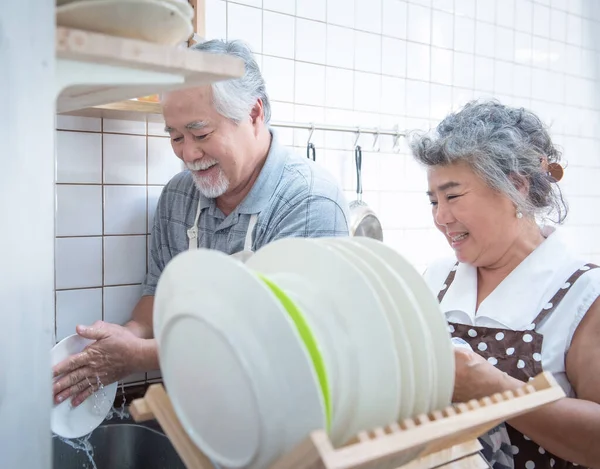 Happy asian elder senior couple washing dishes in sink at home in kitchen at home.