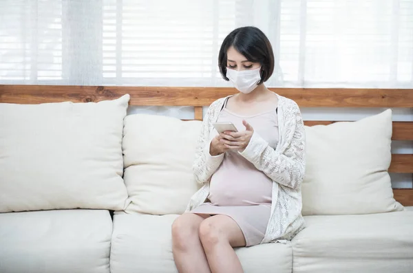 Asyalı hamile kadınlar hastalık nedeniyle maske takıyor, baş dönmesi endişeli akıllı cep telefonu kullanıyor, salgın Wuhan Coronavirüs (COVID-19) sağlık konsepti.