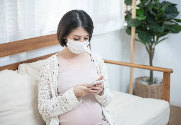 Asyalı hamile kadınlar hastalık nedeniyle maske takıyor, baş dönmesi endişeli akıllı cep telefonu kullanıyor, salgın Wuhan Coronavirüs (COVID-19) sağlık konsepti.