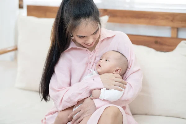 family, child and parenthood concept ,happy beautiful young asian mother smiling hugging holding newborn baby in her arms at home. Mothers day banner with copy space for advertise