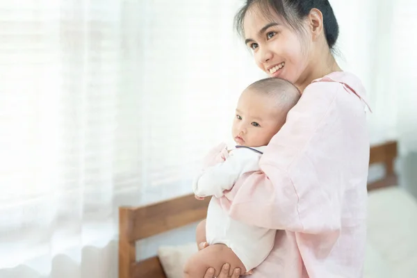 family, child and parenthood concept , happy beautiful young asian mother smiling hugging holding newborn baby in her arms at home. Mothers day banner with copy space for advertise