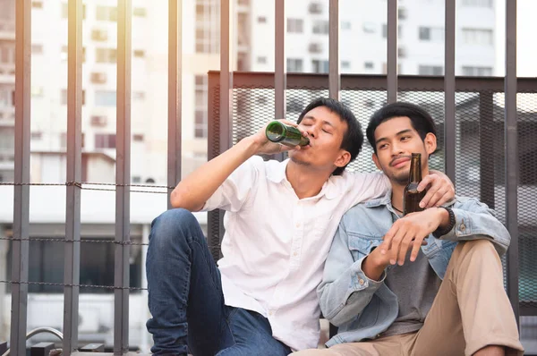 Two young men drunk and sit sleeping on street with bottle of beer