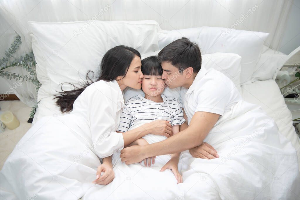 Young asian mother, father and boy sleeping in bed, mom and dad kiss on cheek of son,view from above