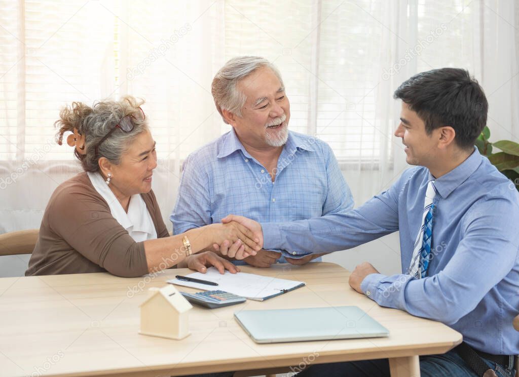 Smiling satisfied senior couple making sale purchase deal concluding contract hand get house key from real estate agent,happy older family and broker shake hands agreeing to buy new house at meeting.