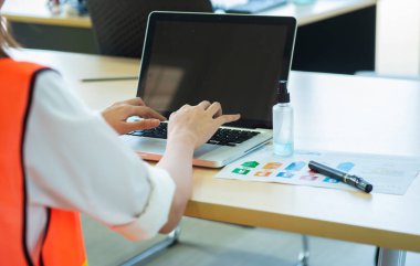 Çalışan genç Asyalı kadının iş yerinde dizüstü bilgisayarda jel alkol spreyi, koronavirüs ya da Cvid-19 yanında, sağlık ve tıp konseptiyle çalışmasının nadir ya da arka görünüşü.