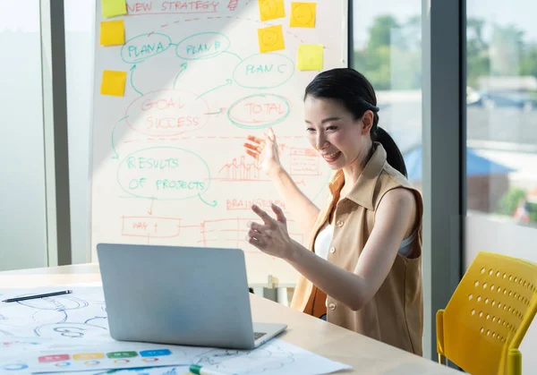 Asyalı güzel girişimci internette bilgisayar ve çizelge tahtası ile ofis veya çalışma masasında çalışıyor, evde çalışıyor ve sosyal uzaklık koronavirüsü veya covid-19 sağlık konseptini koruyor