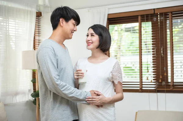 Portrait beautiful young asian couple pregnant woman drink milk dad embracing mom in kitchen. Health care and love of pregnancy mothers day concept.