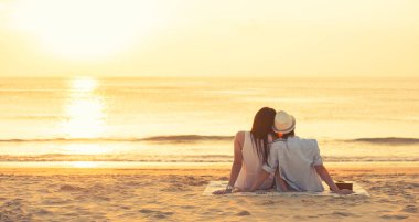 Birbirine aşık çiftler yaz tatilinde sahilde gün batımını izliyorlar. İnsanlar arkada oturup tropikal bir tatil için güneşin batışının tadını çıkarıyorlar. Sahilde romantik bir çift.