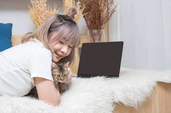 Happy young asian woman with laptop computer petting kitten laying on bed,University colleague student study online with social media,Social distancing, stay at home and work from home concept.