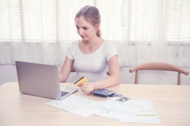 İnternet üzerinden alışveriş yapmak veya kamu hizmetleri faturasını dijital uygulama yoluyla ödemek için kredi kartı tutan beyaz bir genç kadın, evinde kalan akıllı yaşam ve sosyal uzaklık kavramı.