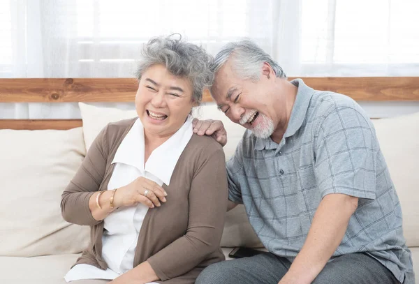 Romantic and happy asian elder senior couple laughing while sitting on sofa at home