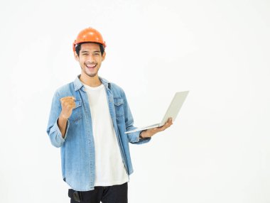 Zeki, genç Asyalı mimar mühendis sıradan kot pantolon ve turuncu güvenlik kaskı giyer. Bu da elinde dizüstü bilgisayarla beyaz arka plan çekimleri üzerinde mutlu ve başarılı bir şekilde çalışmasını kontrol eder..