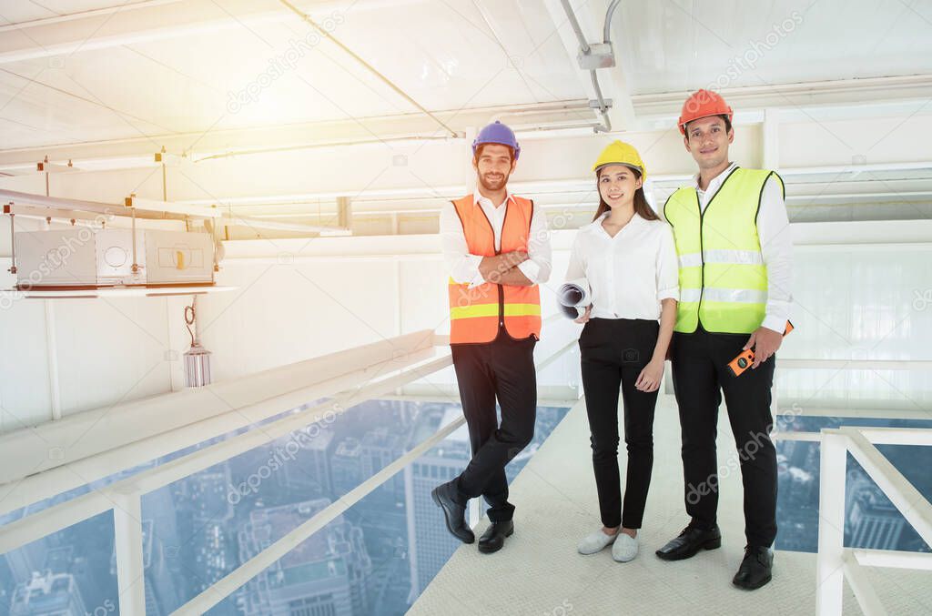Portrait of businessman or engineer architect mixed race young caucasian man and asian woman wear hard hat hand holding blueprint looking at camera at high rise construction site.