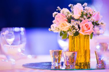 Cam vazo süslemedeki gül çiçekçisi yemek masasında gümüş takımlar ve mum ile iç mekanda dekoratif ışıklar ve güzel bokeh.