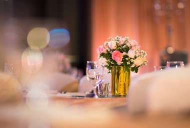 Cam vazo süslemedeki gül çiçekçisi yemek masasında gümüş takımlar ve mum ile iç mekanda dekoratif ışıklar ve güzel bokeh.