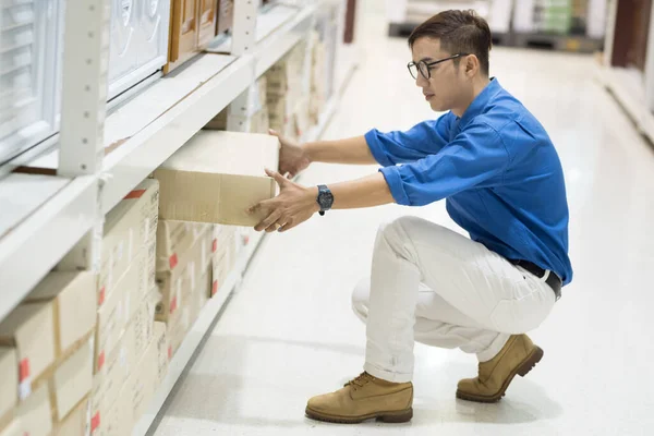 Asian shopper man picking cardboard from hyper market shelf in warehouse.