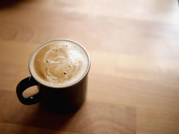 Photo of a small cup of coffee on light brown wooden table.