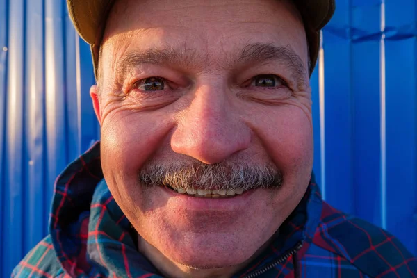 Um homem idoso de boné de beisebol olha e sorri no fundo — Fotografia de Stock