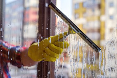 Scraper for washing windows in hands in yellow gloves. clipart