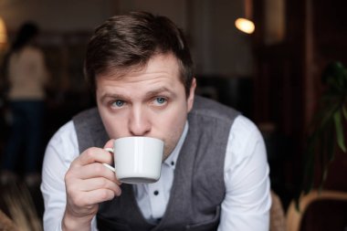 Genç bir adam bir beyaz gömlek ve yelek çay kahvaltılarında ve gün için planları hakkında düşünüyor