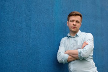 Mavi arka plan üzerinde çapraz elleri olan yakışıklı bir adam portresi portre